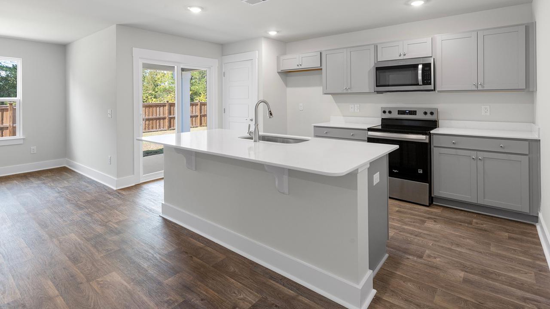 The open-concept family room, kitchen, and dining area feature granite countertops, stainless steel appliances, including a smooth-top range, dishwasher, and overhead microwave.