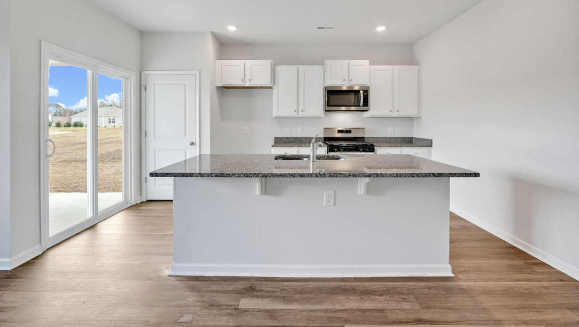 The open-concept family room, kitchen, and dining area feature granite countertops, stainless steel appliances, including a smooth-top range, dishwasher, and overhead microwave.