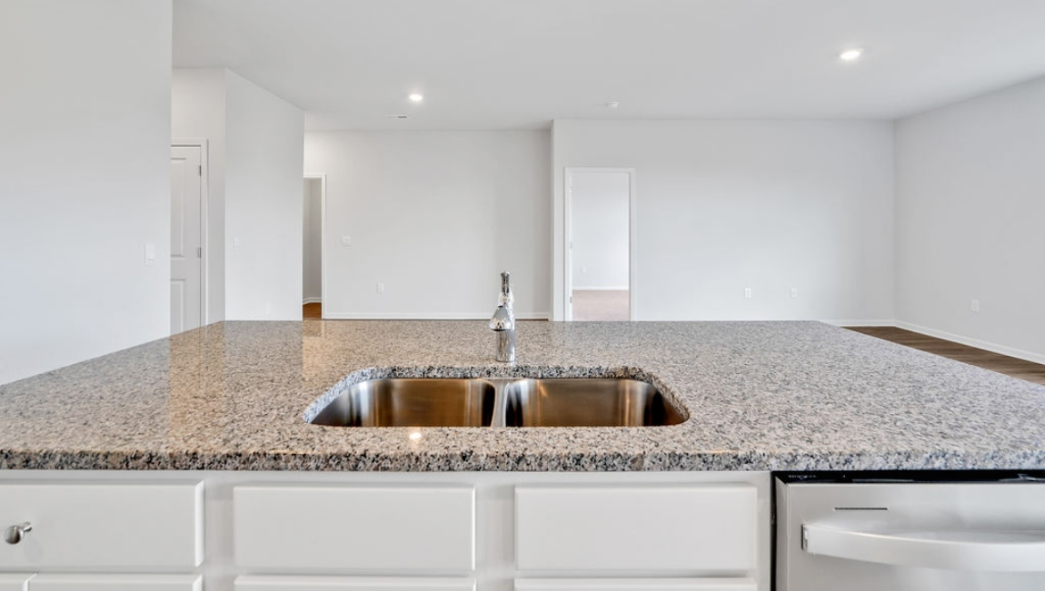 The open-concept family room, kitchen, and dining area feature granite countertops, stainless steel appliances, including a smooth-top range, dishwasher, and overhead microwave.