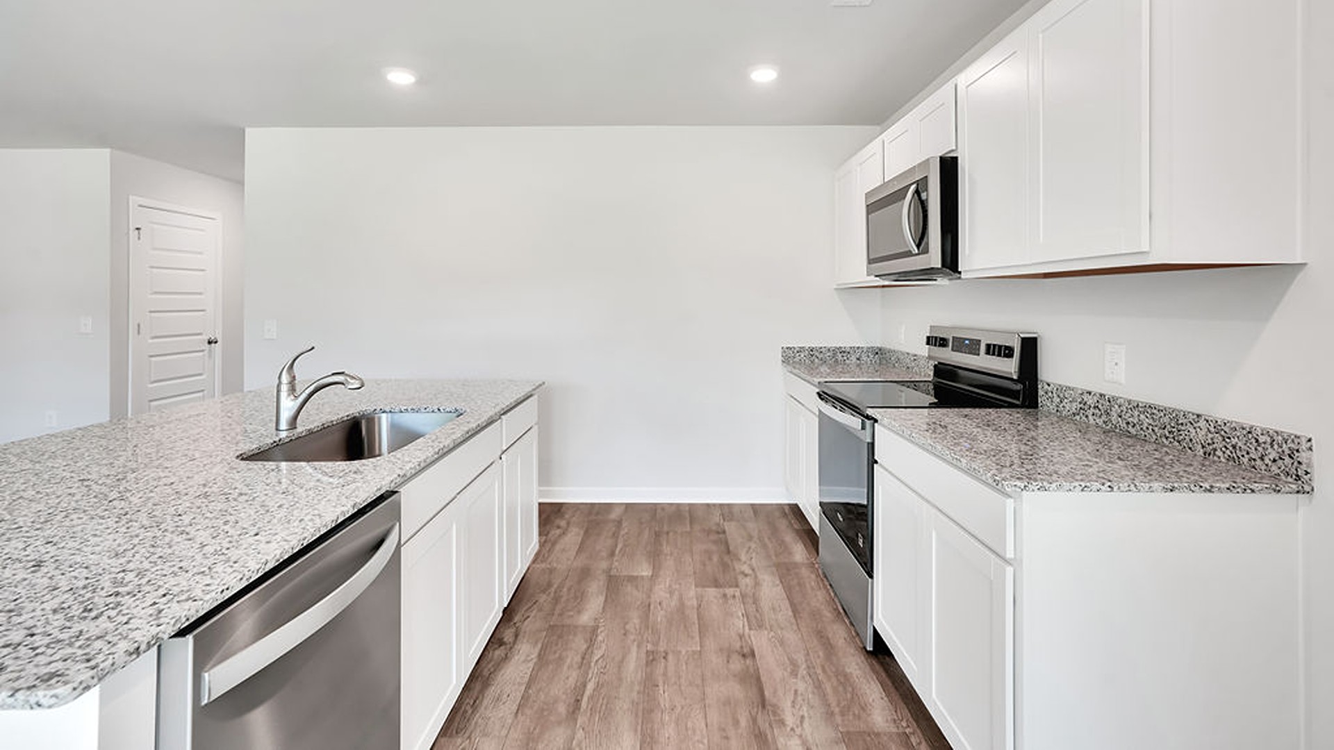 The open-concept family room, kitchen, and dining area feature granite countertops, stainless steel appliances, including a smooth-top range, dishwasher, and overhead microwave.
