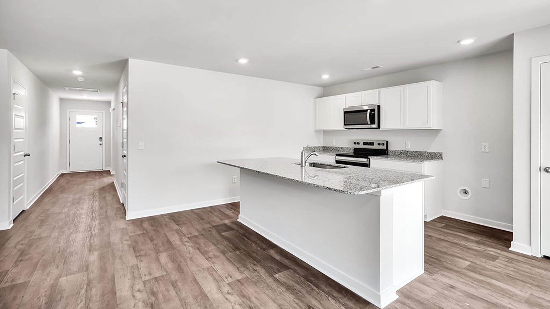 The open-concept family room, kitchen, and dining area feature granite countertops, stainless steel appliances, including a smooth-top range, dishwasher, and overhead microwave.