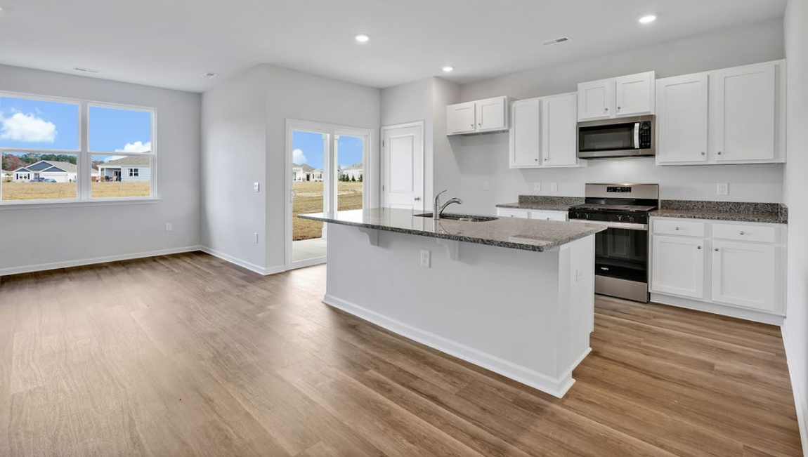 The open-concept family room, kitchen, and dining area feature granite countertops, stainless steel appliances, including a smooth-top range, dishwasher, and overhead microwave.
