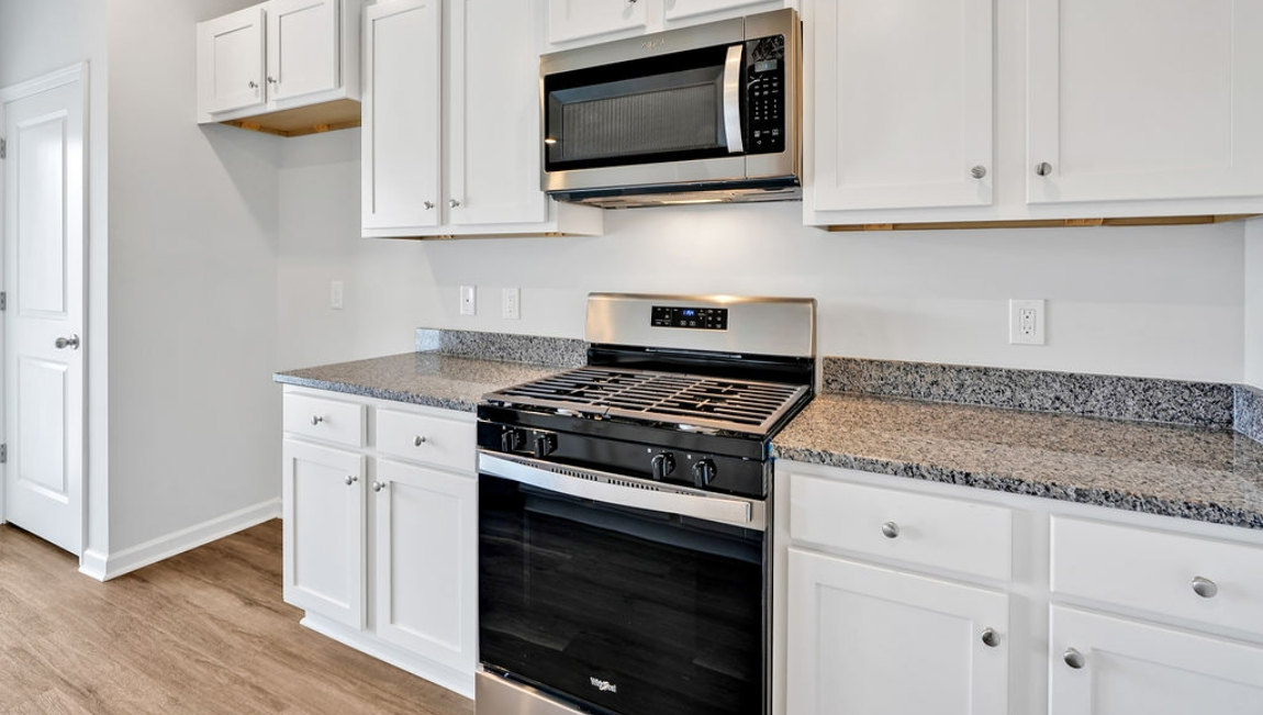 The open-concept family room, kitchen, and dining area feature granite countertops, stainless steel appliances, including a smooth-top range, dishwasher, and overhead microwave.