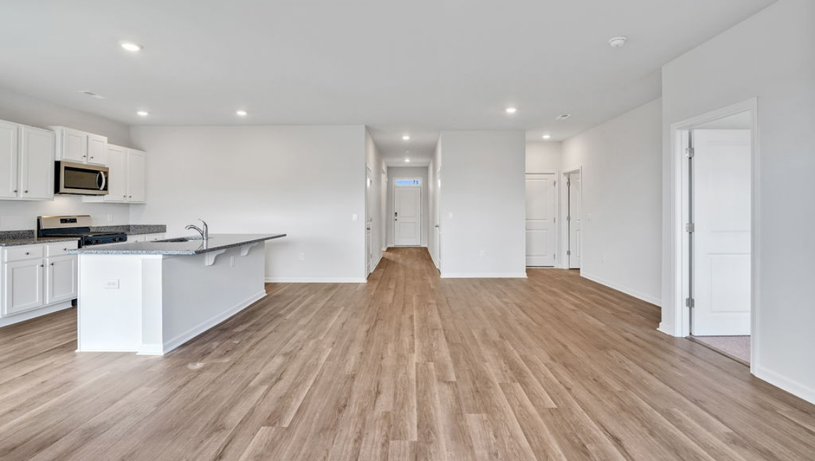 The open-concept family room, kitchen, and dining area feature granite countertops, stainless steel appliances, including a smooth-top range, dishwasher, and overhead microwave.