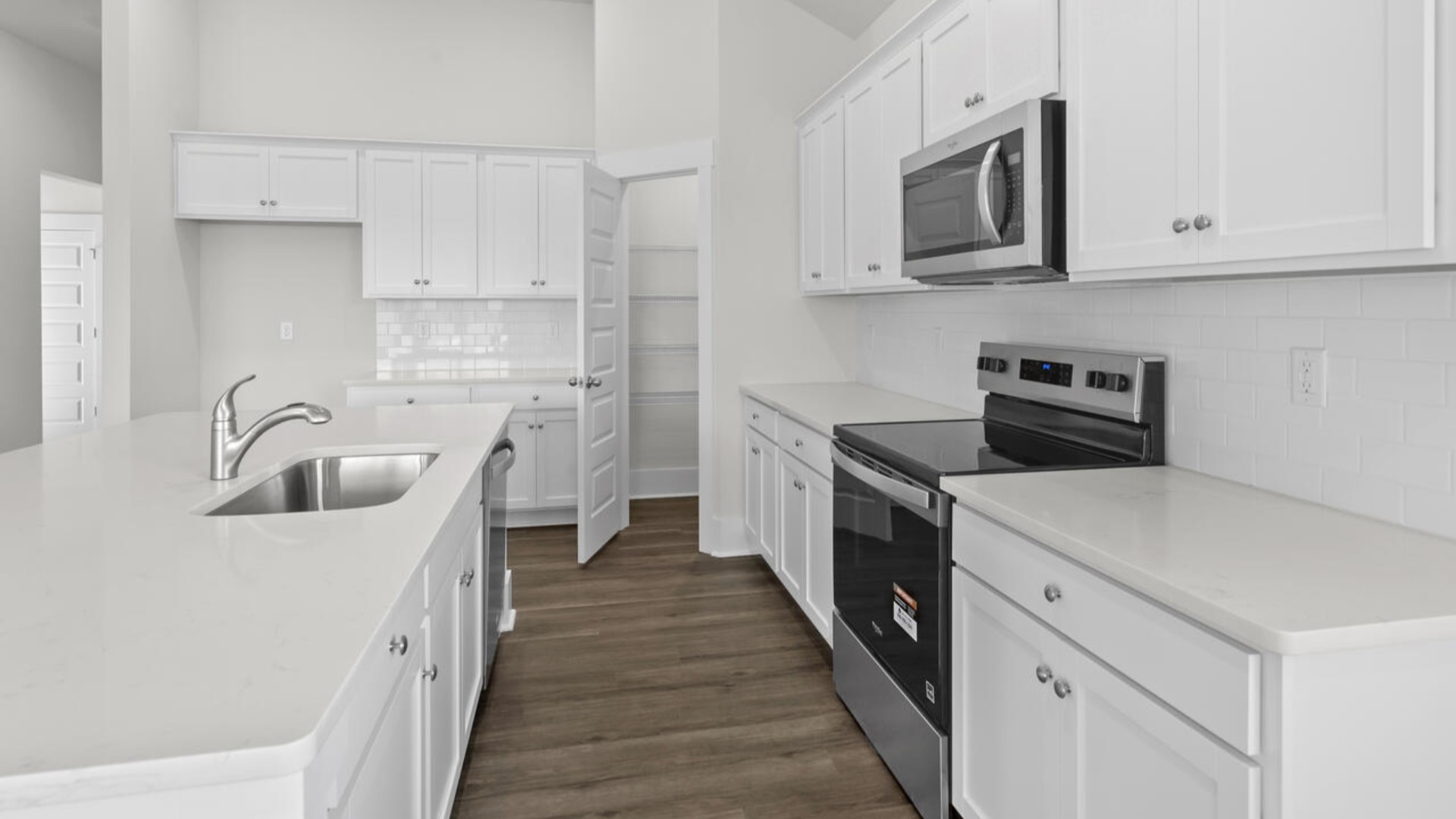 A large gourmet kitchen that features a large island, quartz countertops, walk-in pantry, and stainless-steel appliances. Luxury Vinyl Plank flooring is included throughout the home, giving you a wood-like look with the durability to handle all your beach days