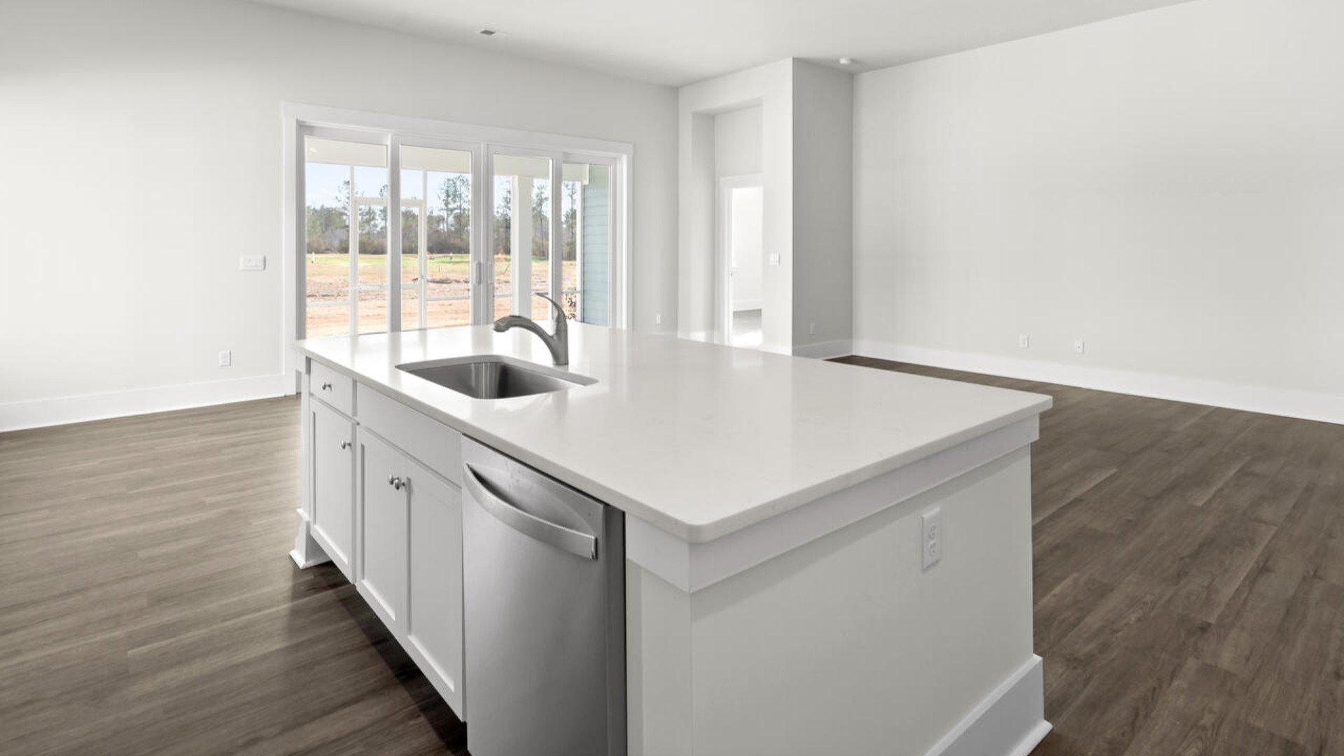 A large gourmet kitchen that features a large island, quartz countertops, walk-in pantry, and stainless-steel appliances. Luxury Vinyl Plank flooring is included throughout the home, giving you a wood-like look with the durability to handle all your beach days