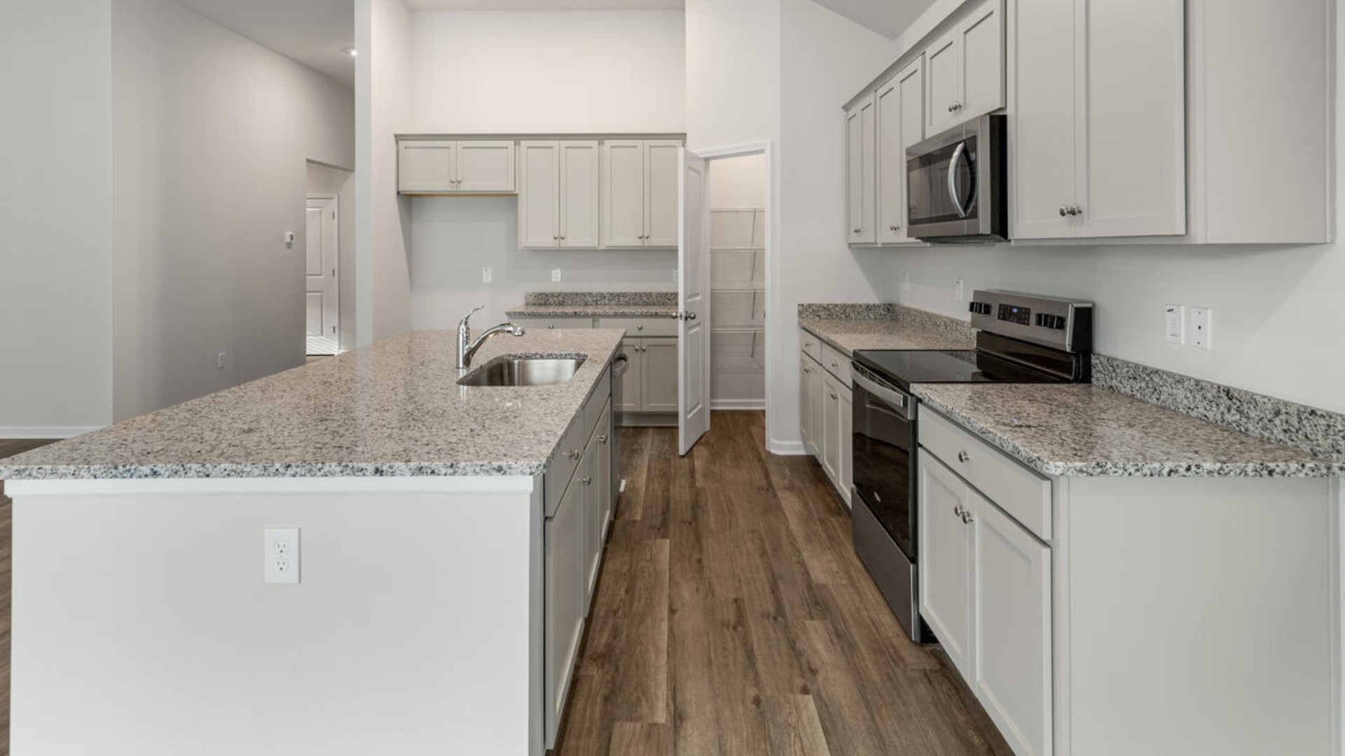 A large gourmet kitchen that features a large island, granite countertops, walk-in pantry, and stainless-steel appliances. Luxury Vinyl Plank flooring is included throughout the home, giving you a wood-like look with the durability to handle all your beach days