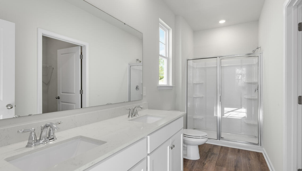 New Homes in Leland NC. The Kerry floor plan offers open living space and a 2-car garage. At the front are two guest bedrooms and a full bathroom, perfect for visitors or a home office. The open-concept family room, kitchen, and dining area feature Granite countertops, stainless steel appliances, including a smooth-top range, dishwasher and overhead microwave