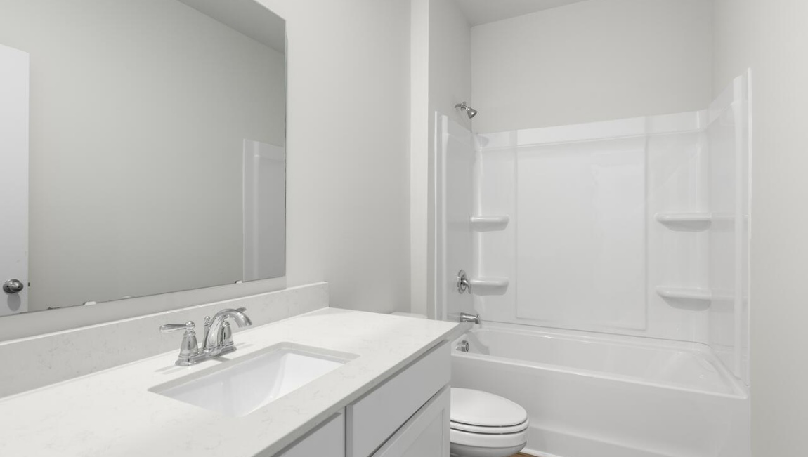 New Homes in Leland NC. The Kerry floor plan offers open living space and a 2-car garage. At the front are two guest bedrooms and a full bathroom, perfect for visitors or a home office. The open-concept family room, kitchen, and dining area feature Granite countertops, stainless steel appliances, including a smooth-top range, dishwasher and overhead microwave