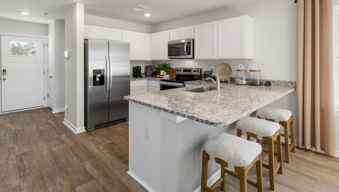 a spacious kitchen that flows into a light-filled living area, perfect for hosting guests. The kitchen is equipped with stainless steel appliances and granite countertops.