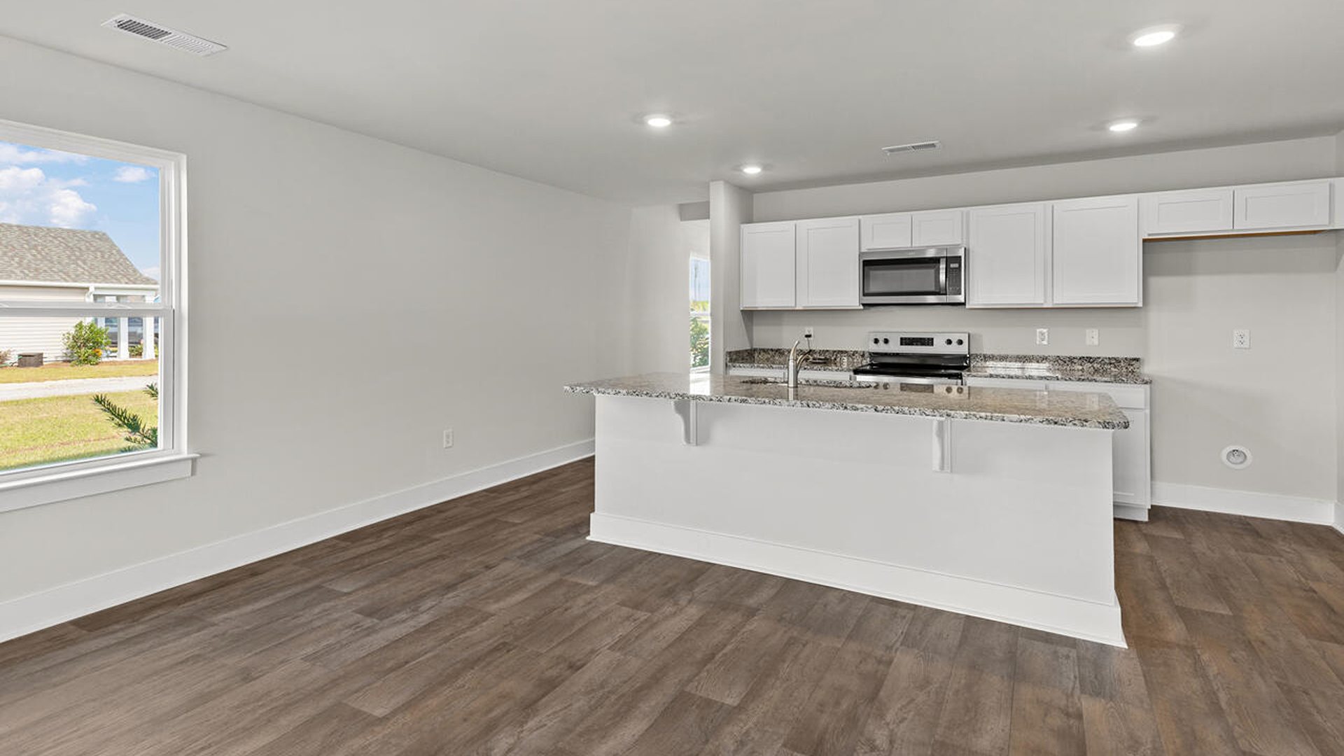 This beautiful kitchen features white cabinetry, granite counters, a large kitchen island with room for 4 counter height barstools and there's a pantry too. You’ll never be too far from the action with the living and dining area right there.