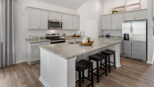 large gourmet kitchen with 36'' staggered cabinets with crown molding, granite, tile backsplash, walk-in pantry, and stainless-steel appliances in kitchen.