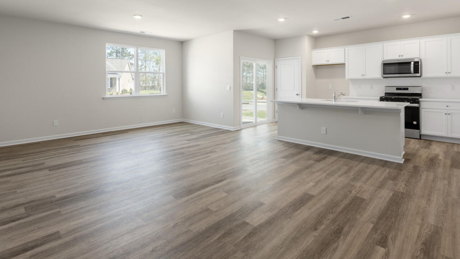 The open-concept family room, kitchen, and dining area feature granite countertops, stainless steel appliances, including a smooth-top range, dishwasher and overhead microwave.