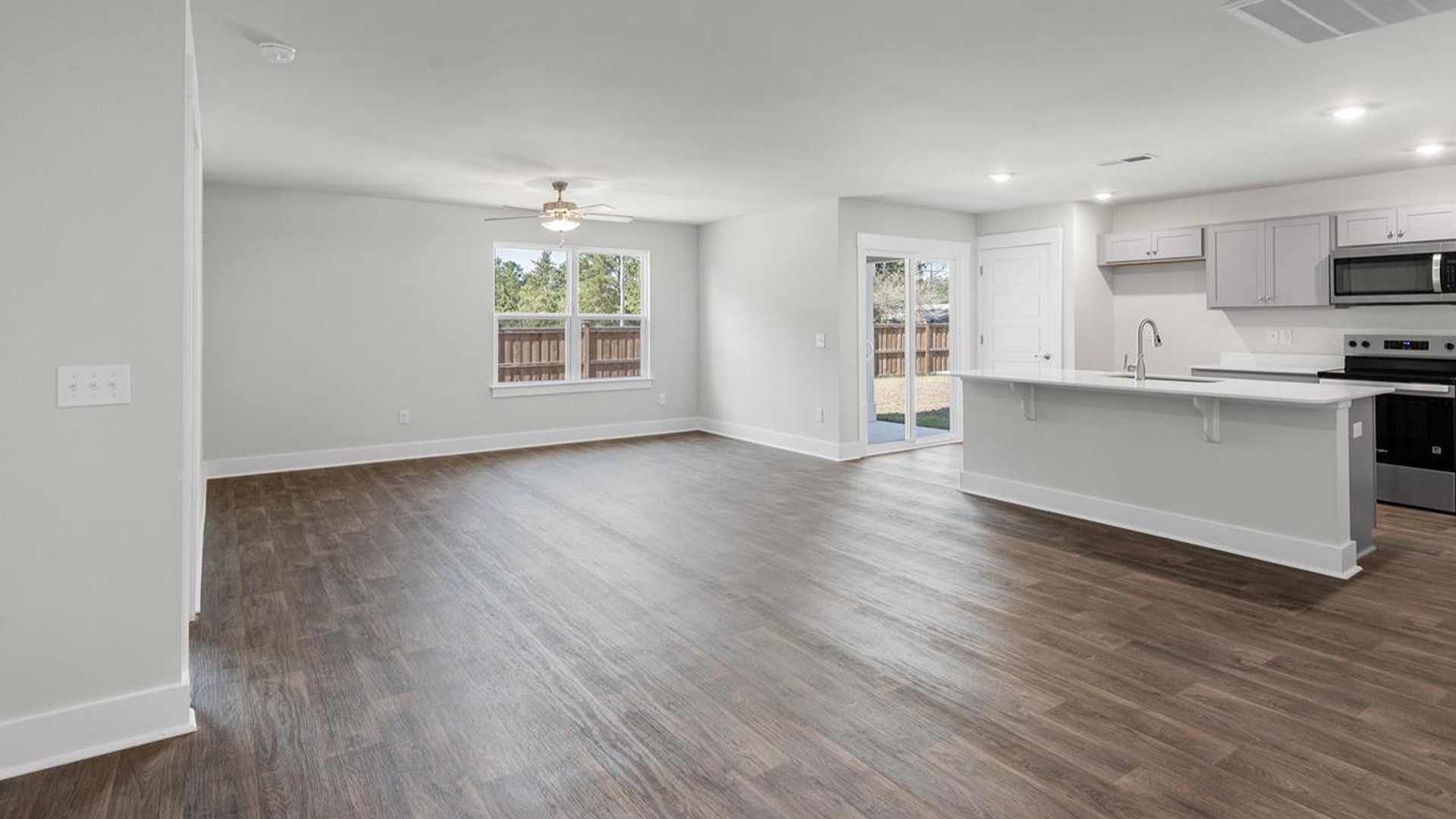 The open-concept family room, kitchen, and dining area feature granite countertops, stainless steel appliances, including a smooth-top range, dishwasher and overhead microwave.
