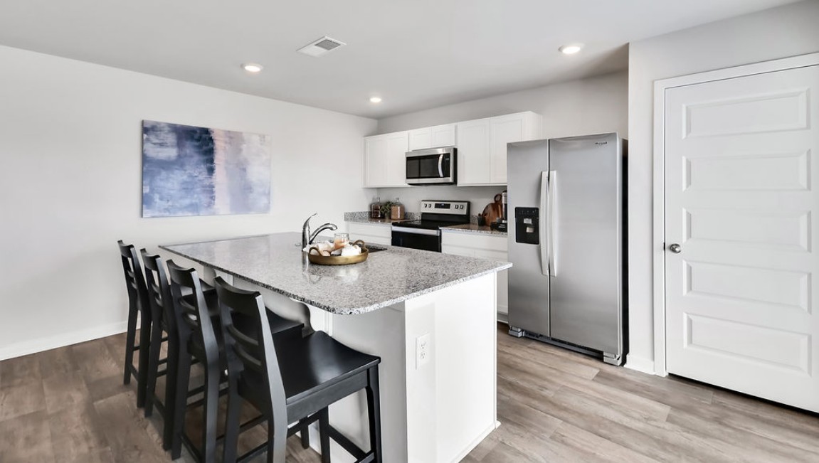 The open-concept family room, kitchen, and dining area feature granite countertops, stainless steel appliances, including a smooth-top range, dishwasher, and overhead microwave.