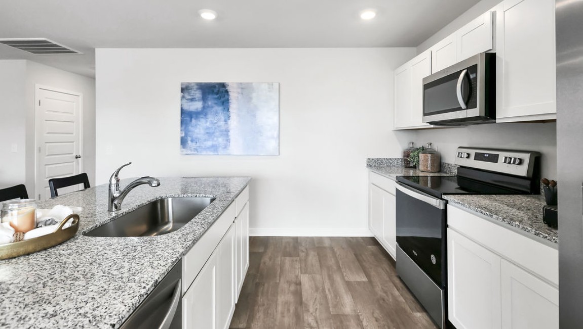 The open-concept family room, kitchen, and dining area feature granite countertops, stainless steel appliances, including a smooth-top range, dishwasher, and overhead microwave.
