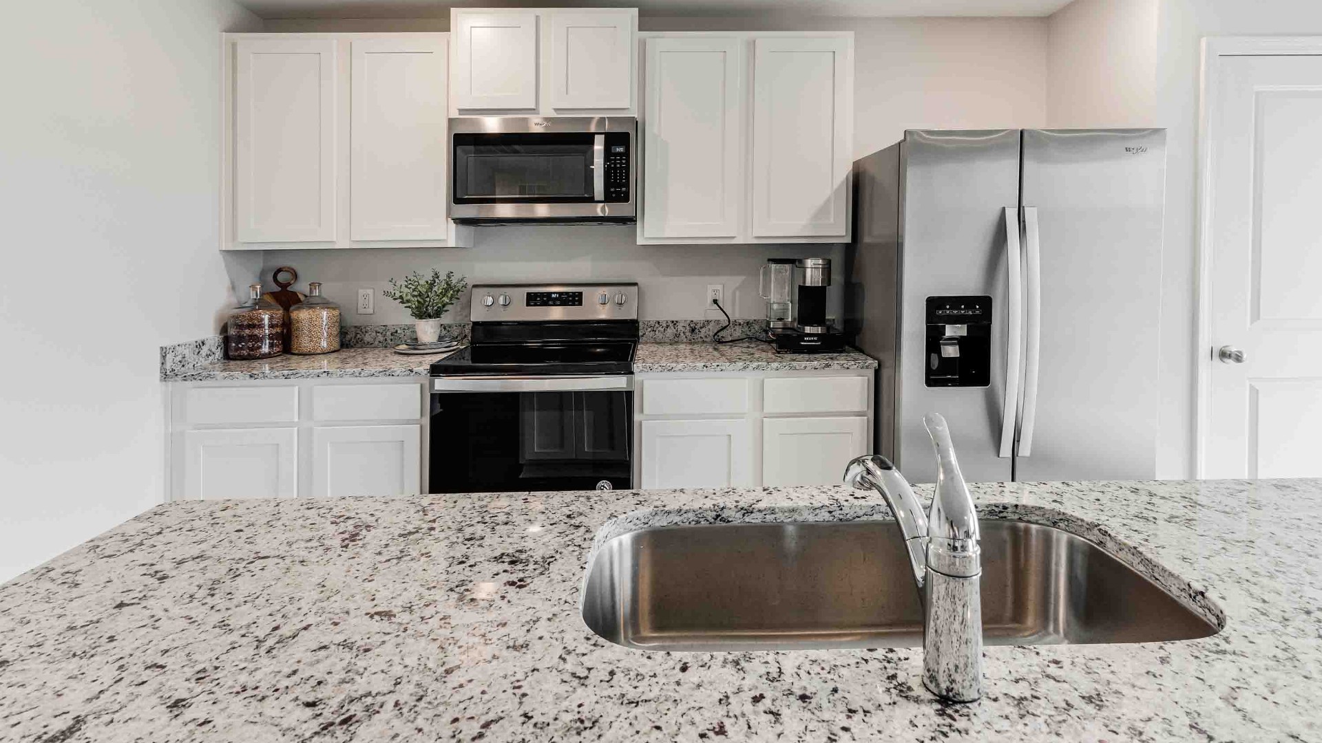 At the front are two guest bedrooms and a full bathroom, perfect for visitors or a home office. The open-concept family room, kitchen, and dining area feature granite countertops, stainless steel appliances, including a smooth-top range, dishwasher, and overhead microwave.