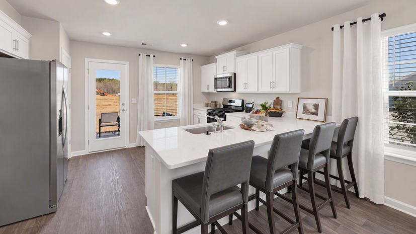 Kitchen space at the back of the new construction home with a kitchen bar and access to the back patio through back door