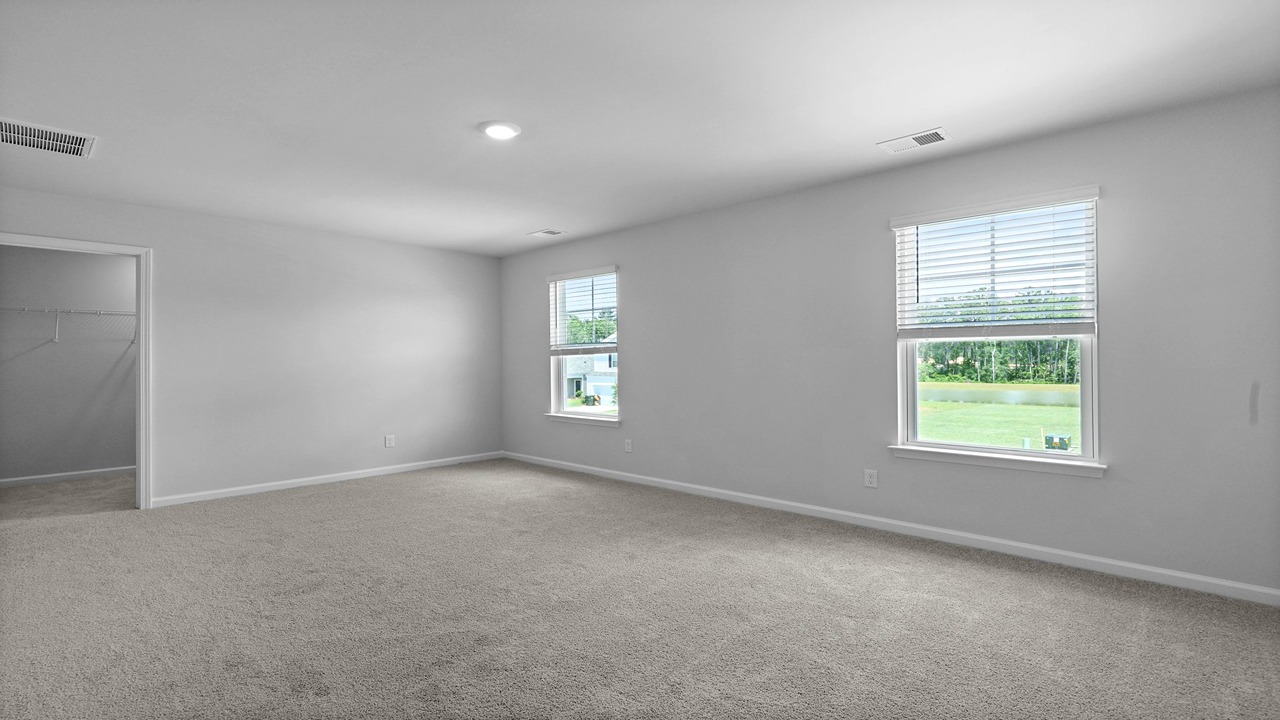Spacious primary bedroom with natural light and carpet flooring