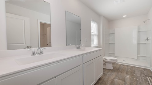 There are double sinks and grey cabinetry in the primary bathroom.