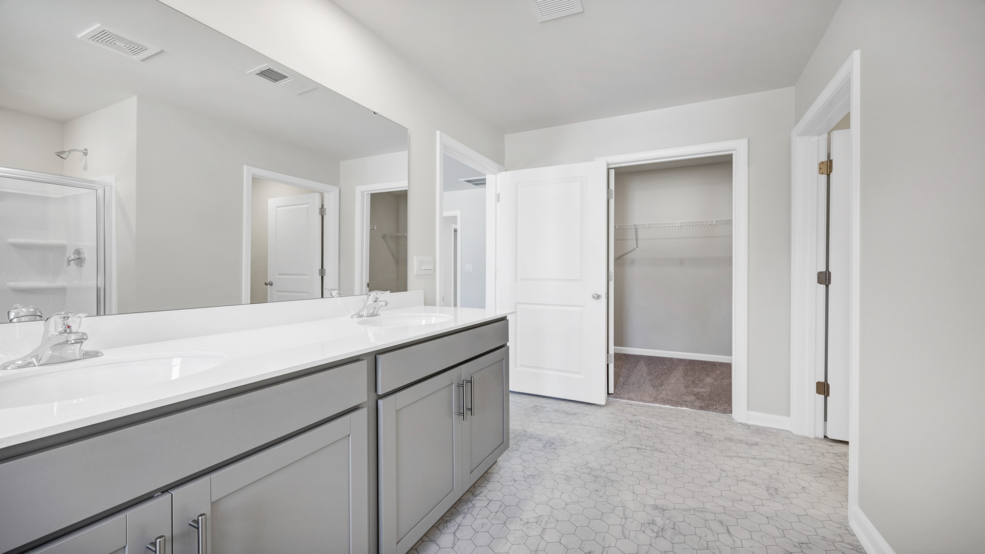 En-suite primary bathroom with double vanity and gray cabintery