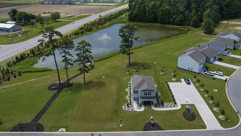 Model home near pond with landscaping and a parking area