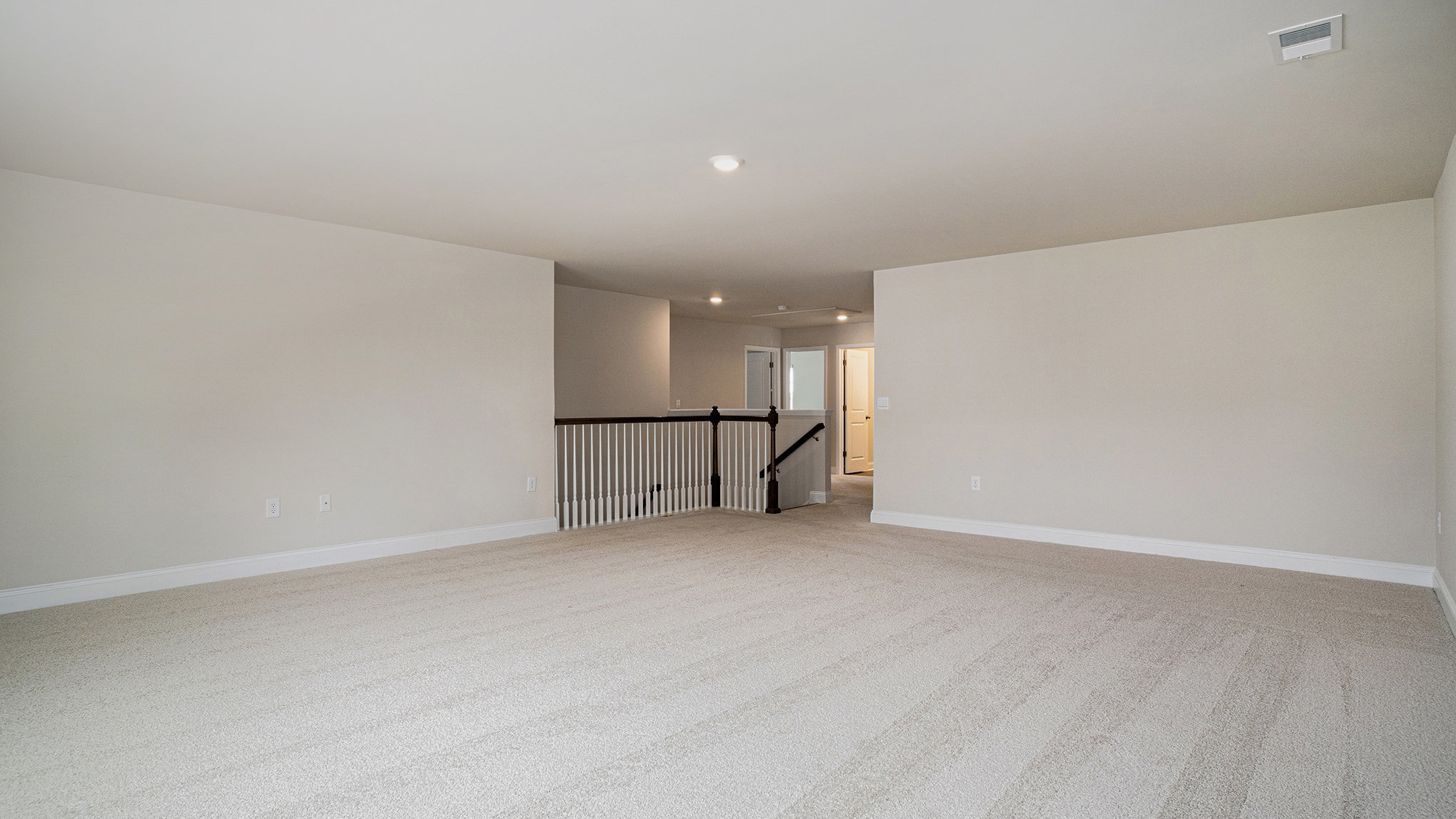 Large loft space at the top of the stairs with carpet flooring and natural light
