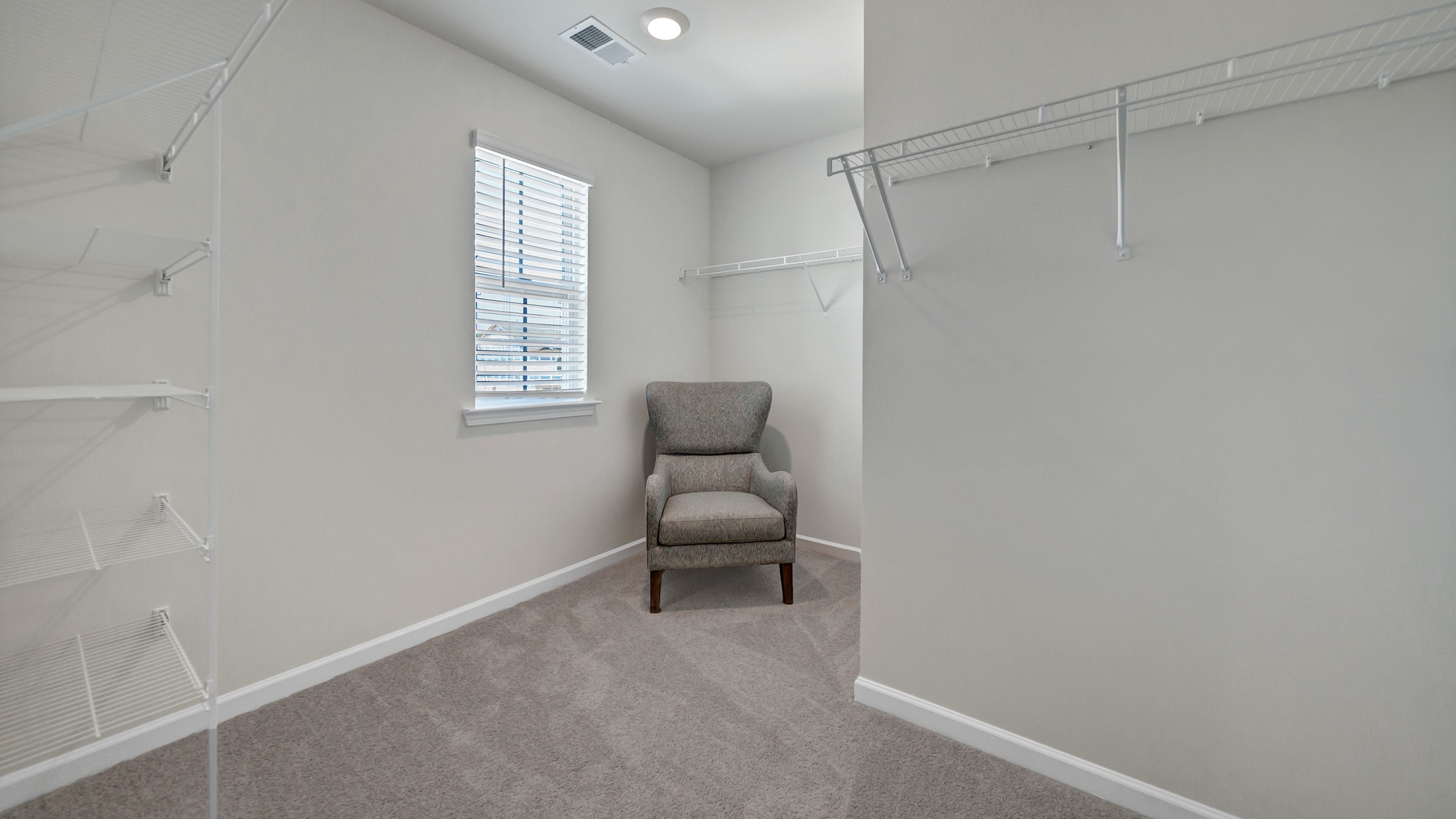 Walk-in primary closet with a window and room for seating
