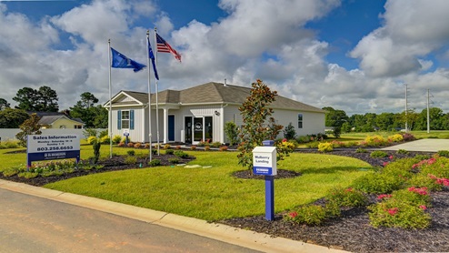 The model home features informational signage and flags outside.