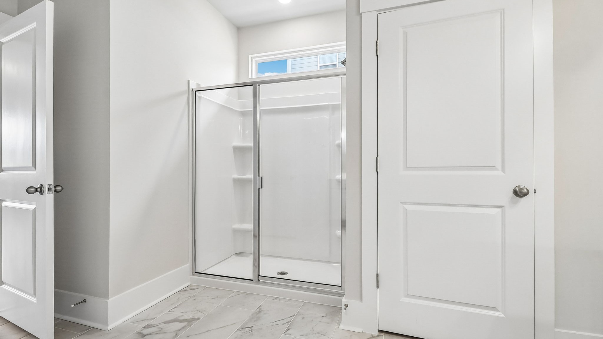 Standup primary shower with glass front and tile bathroom flooring