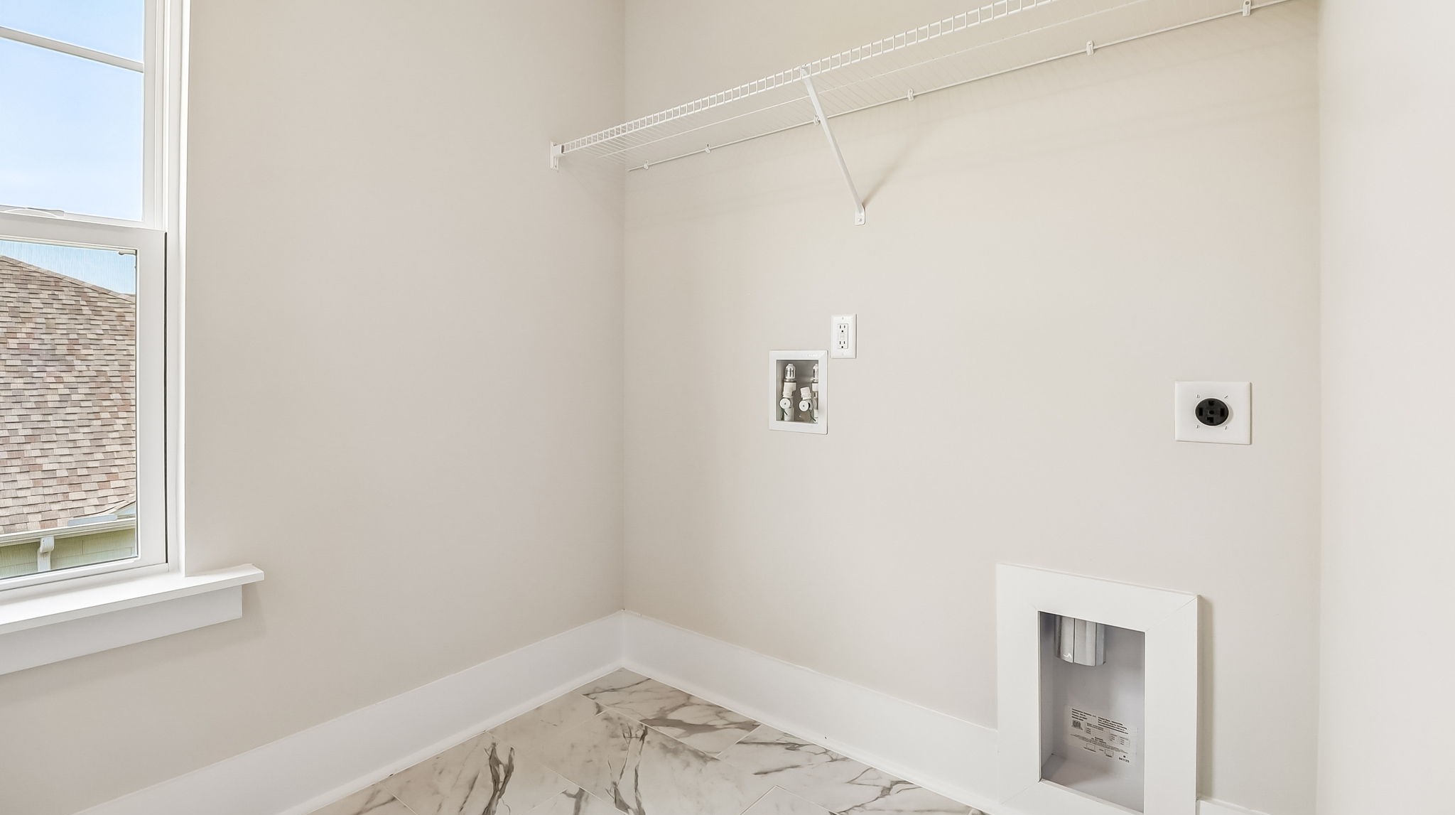 Laundry room upstairs in new construction home with a window for light, tile flooring, and shelving