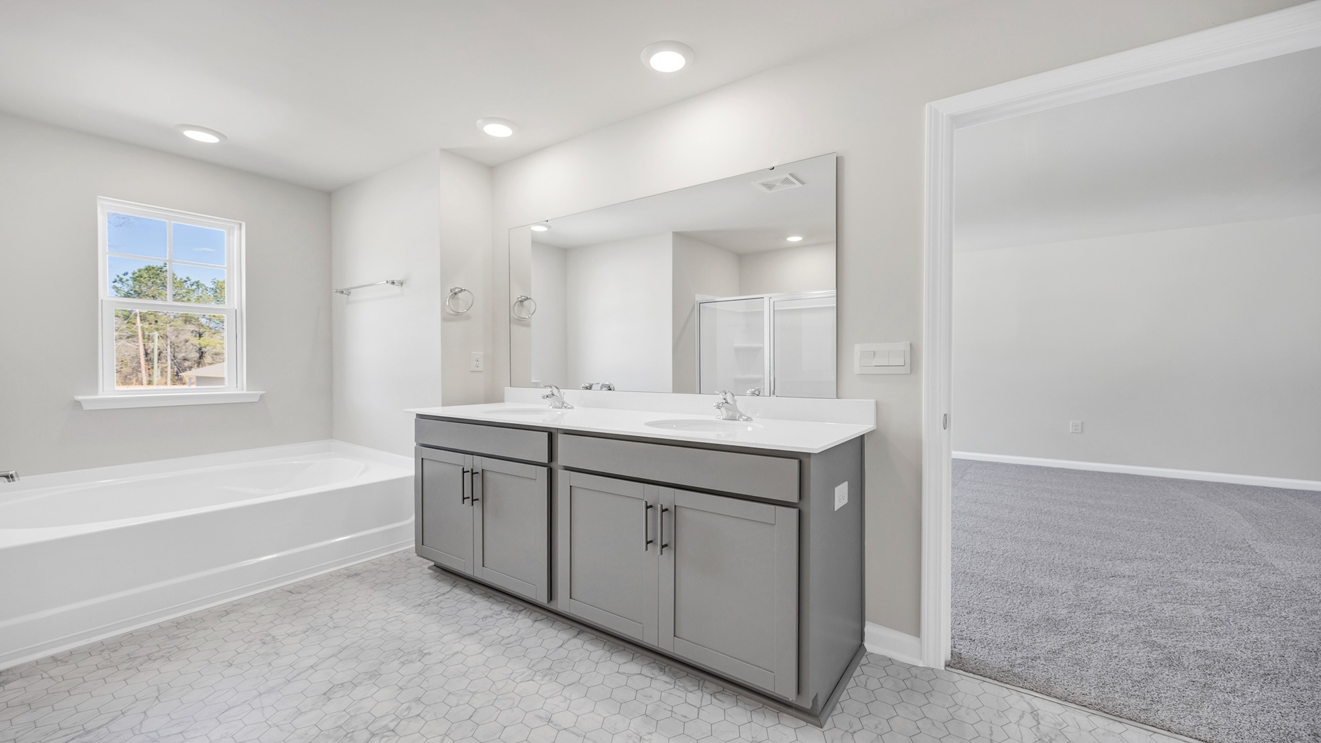 There are double sinks and grey cabinetry in the primary bathroom.