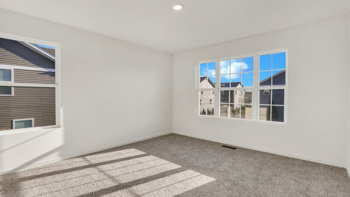 Primary bedroom in this townhome features double windows, soft carpet, walk-in closet, a private spa-inspired ensuite bath