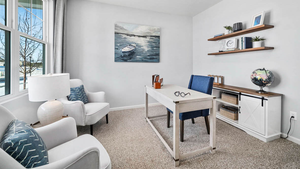 Front room of home staged as an office with carpeted floors and a large window.