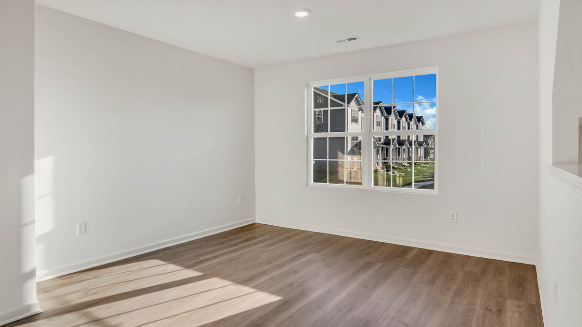 Spacious living room with brown flooring, white walls and windows