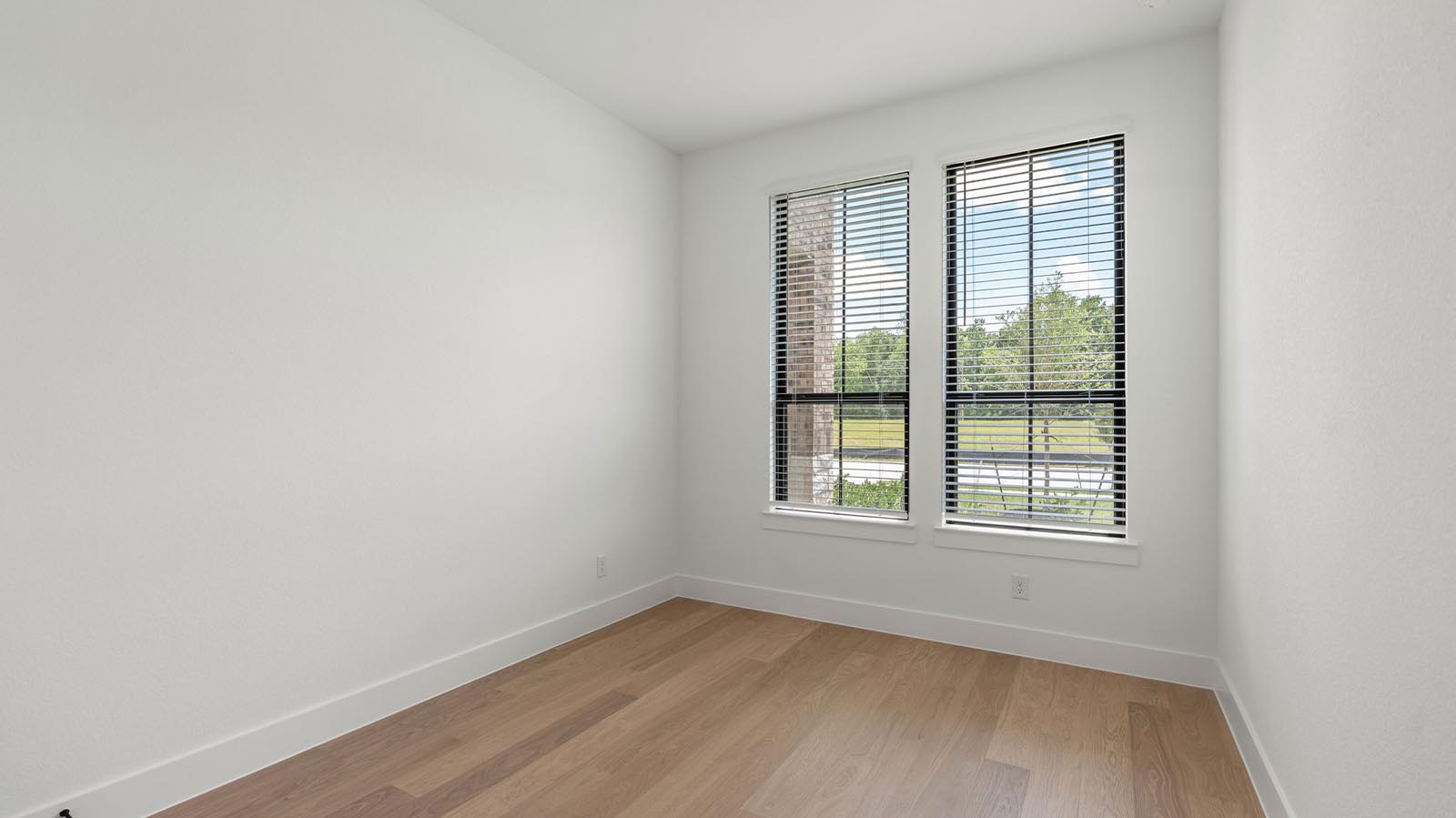 A third bedroom with two windows, decorated with bedroom furniture and wood flooring.