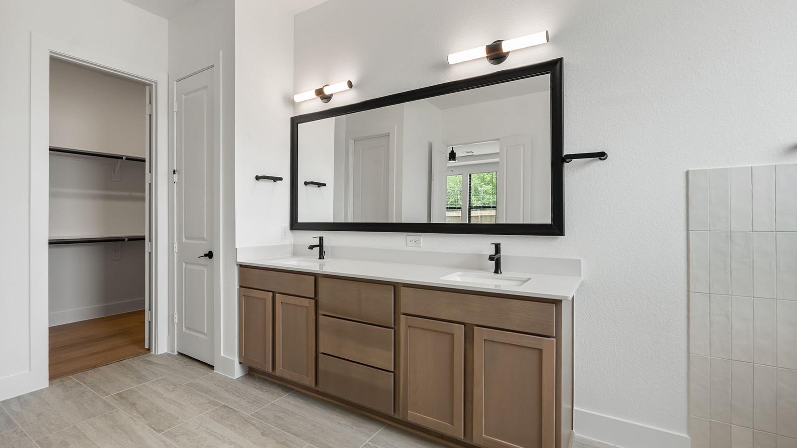 Luxurious primary bathroom with dual vanities, a soaking tub, and a walk-in closet