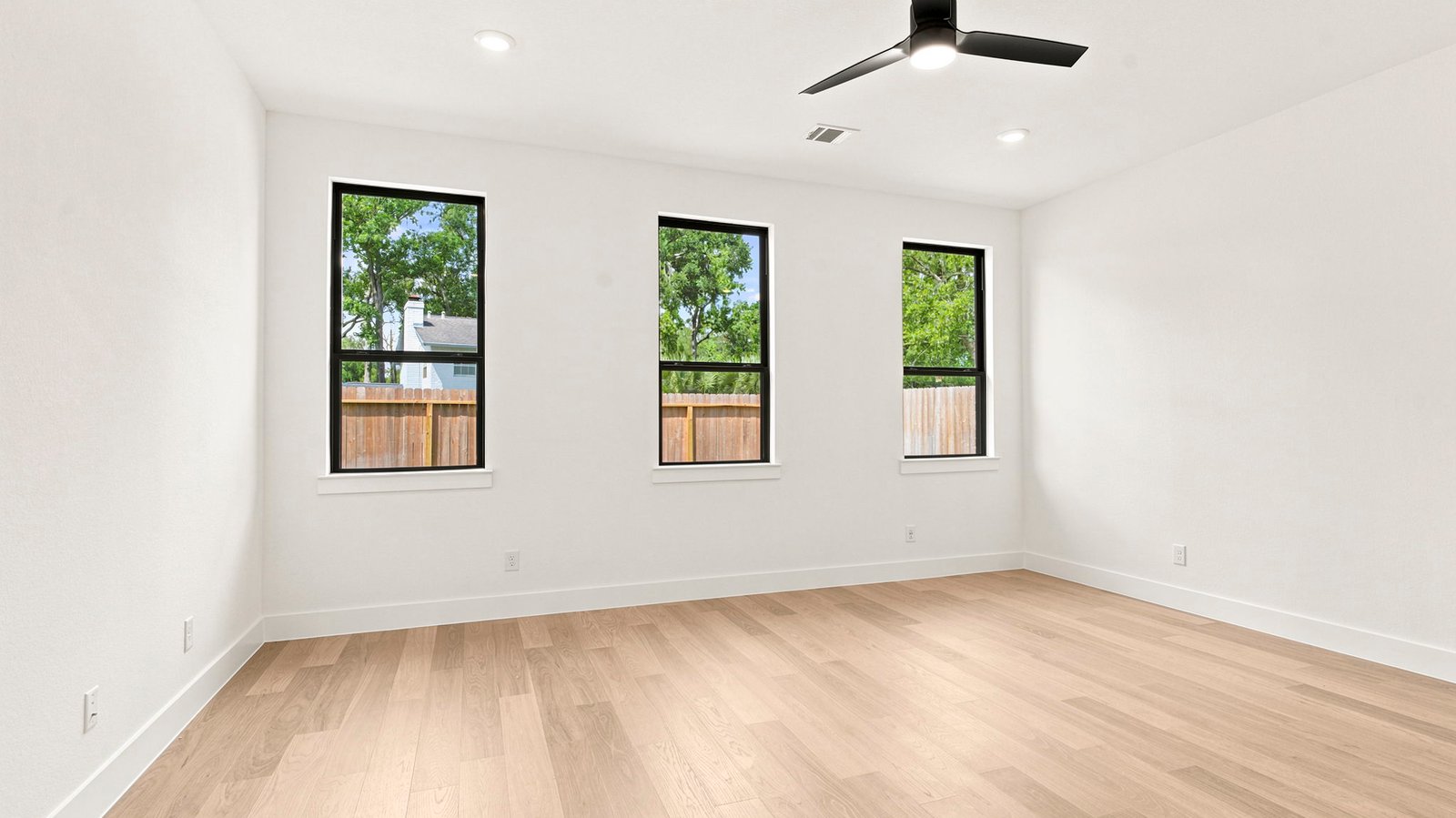 The primary bedroom with ceiling fan, three large windows for natural lighting, hardwood floors, and a large walk-in closet.