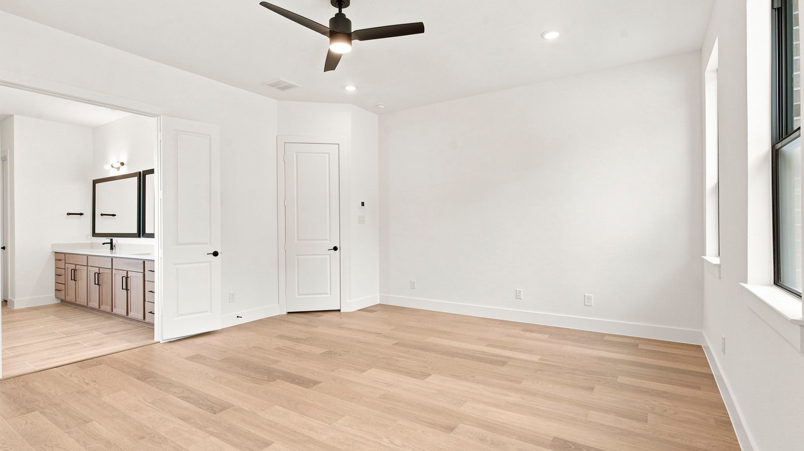 The primary bedroom with ceiling fan, three large windows for natural lighting, hardwood floors, and a large walk-in closet.