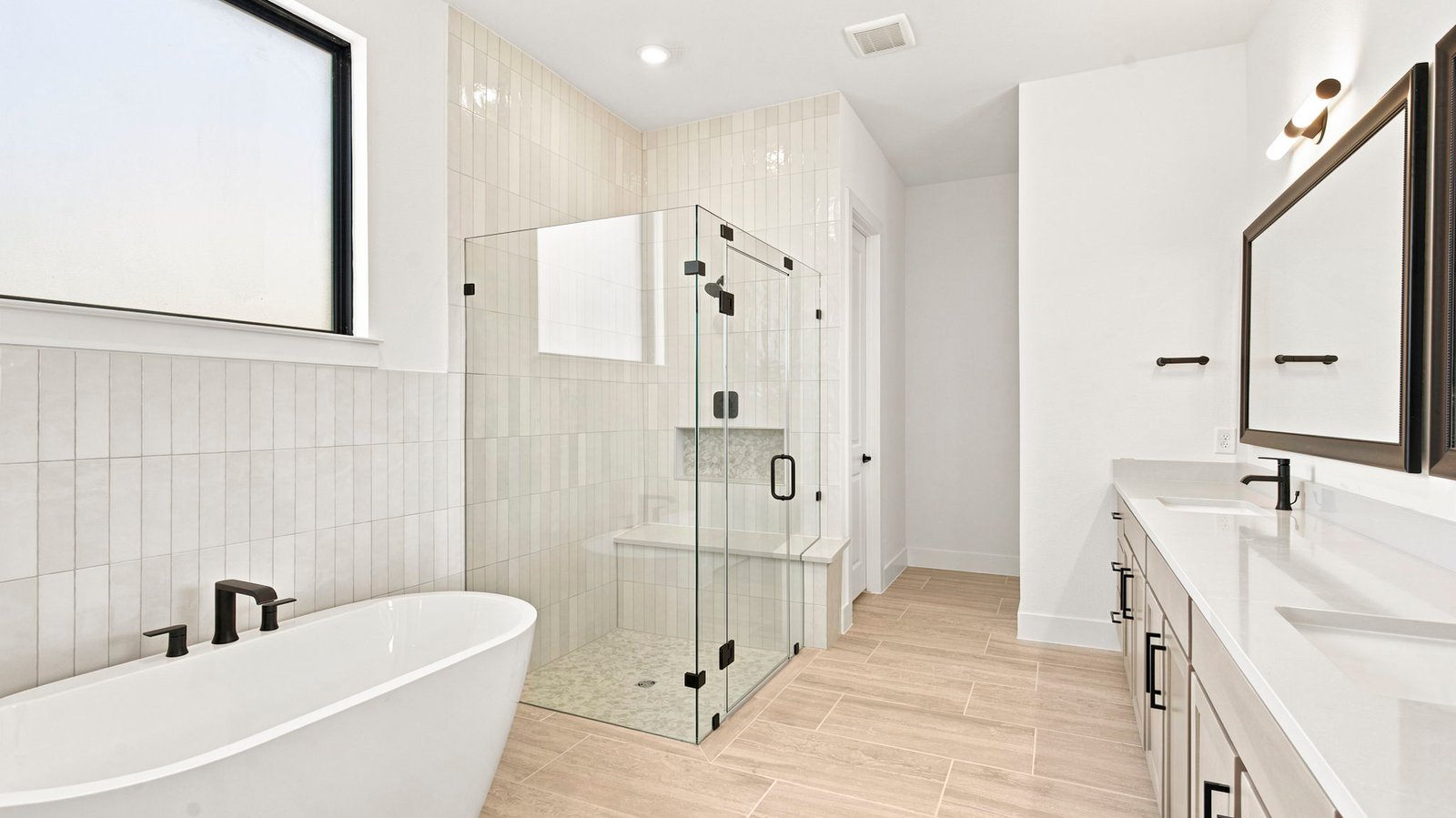 Luxurious primary bathroom with dual vanities, a soaking tub, and separate glass-enclosed walk in shower