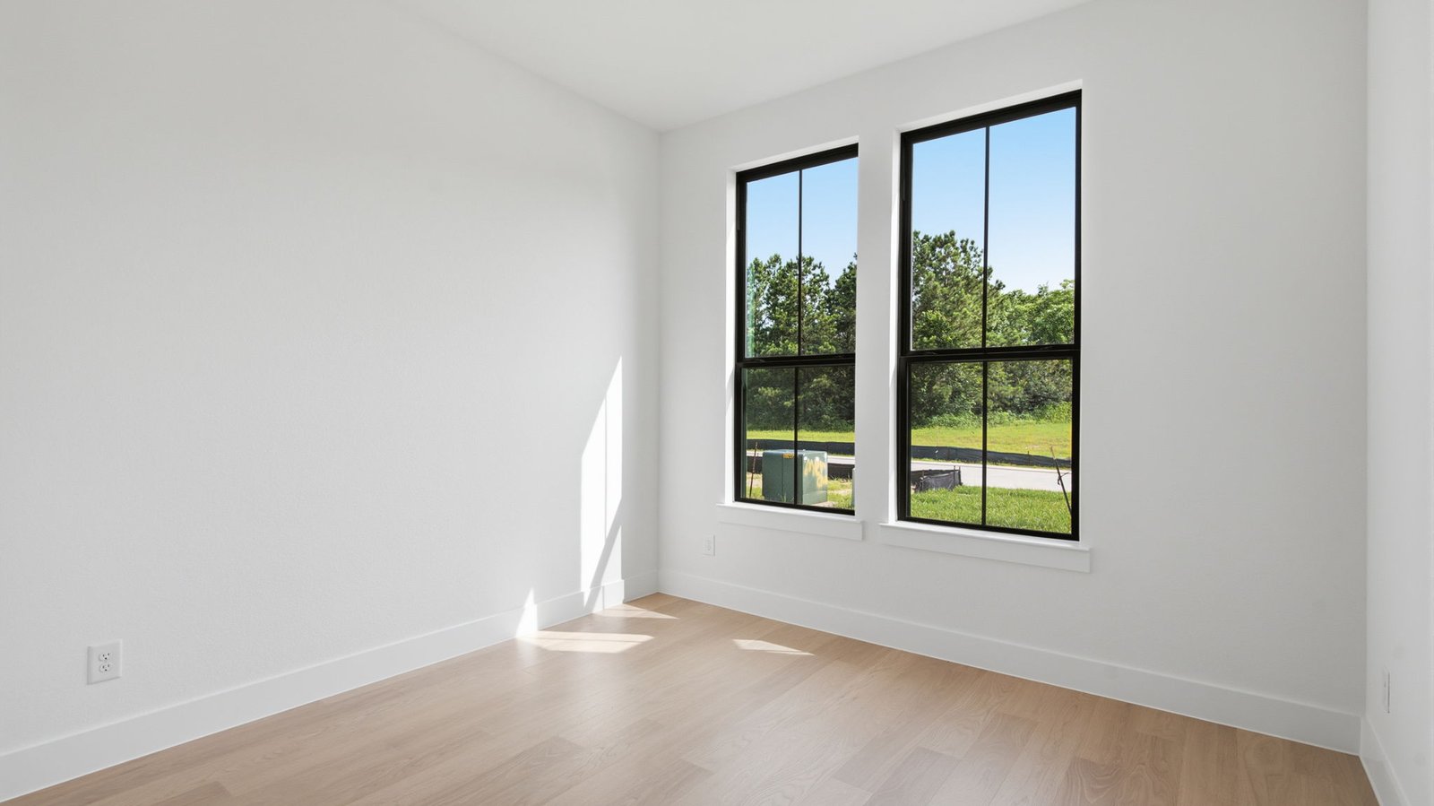 A secondary bedroom with two large windows, neutral painted walls, and wood flooring.
