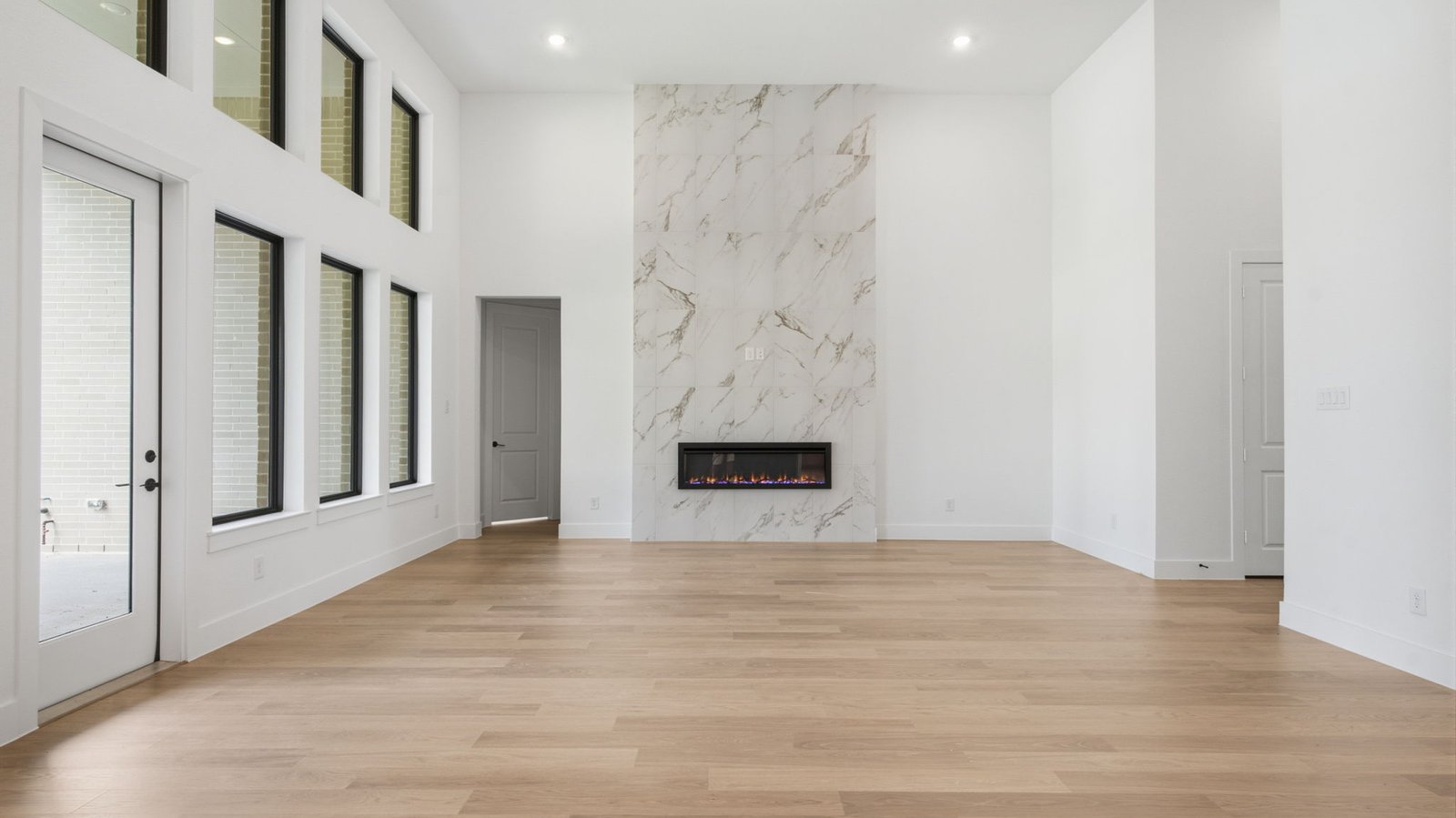 Elegant living room with soaring ceilings, a cozy electric fireplace, open-concept design, and seamless flow into a chef-inspired kitchen.