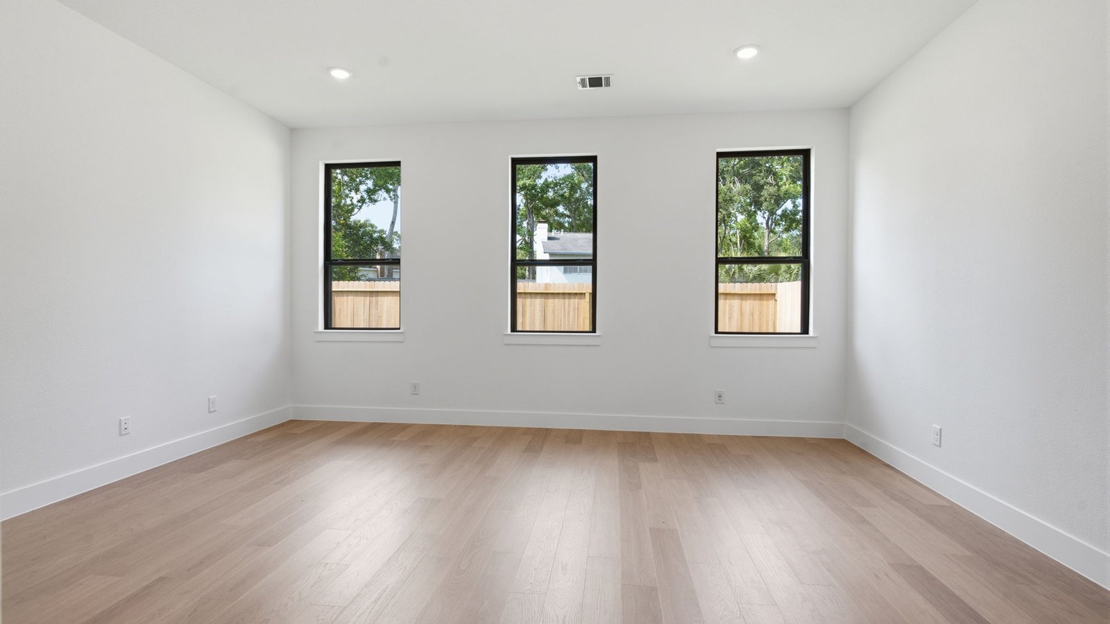 The primary bedroom with ceiling fan, three large windows for natural lighting, hardwood floors, and a large walk-in closet.