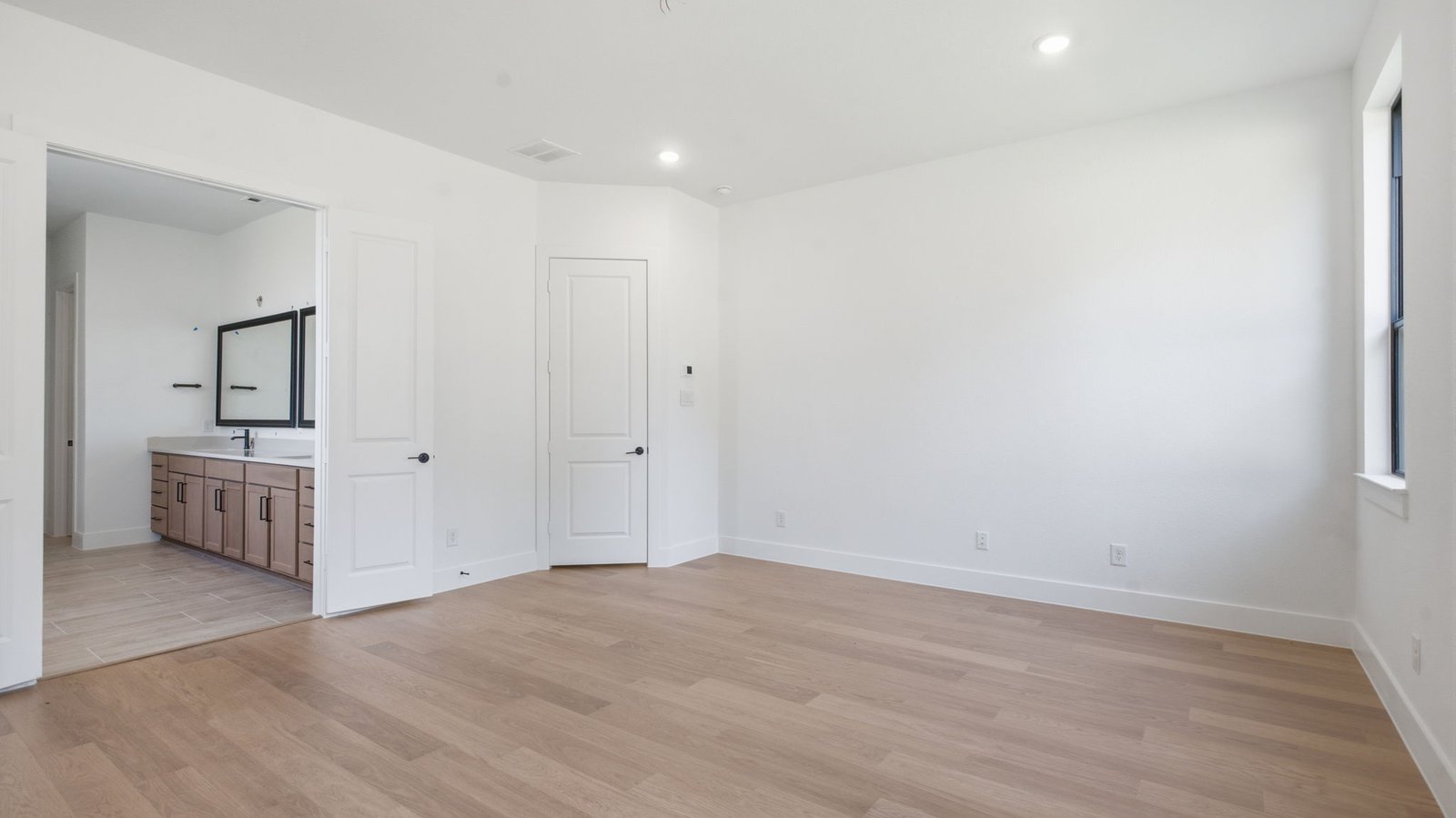 The primary bedroom with ceiling fan, three large windows for natural lighting, hardwood floors, and a large walk-in closet.