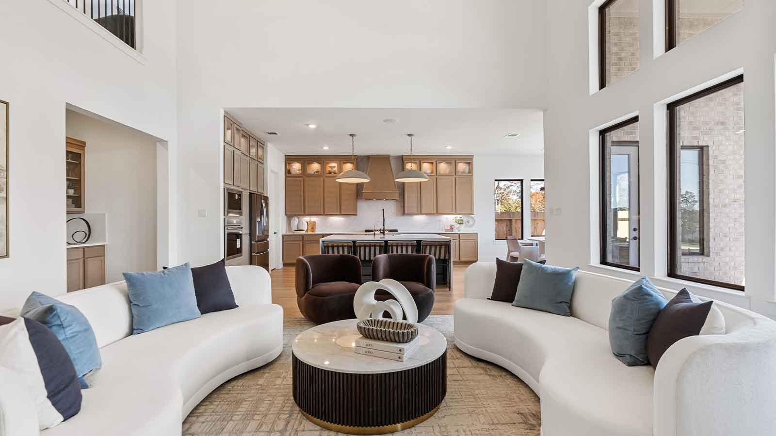 A luxurious living room featuring tall ceilings, large windows for natural lighting wood flooring and a view to the backyard.