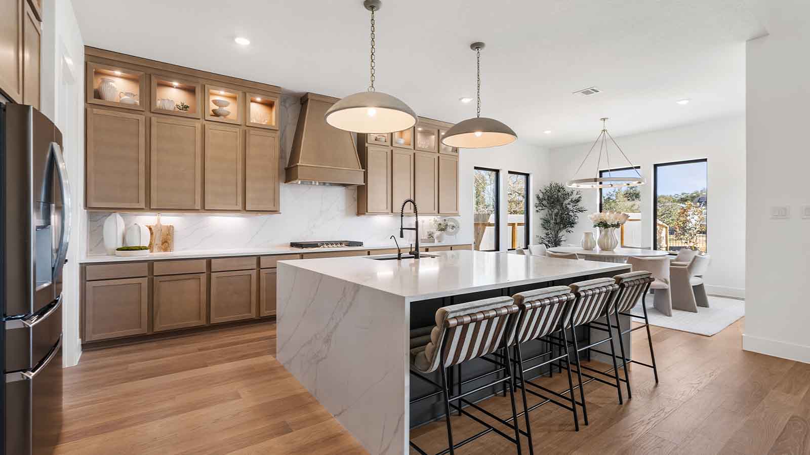 Luxurious and spacious kitchen with quartz countertops, stainless steel appliances, wood cabinets with natural stain, expansive storage and an island with bar seating.
