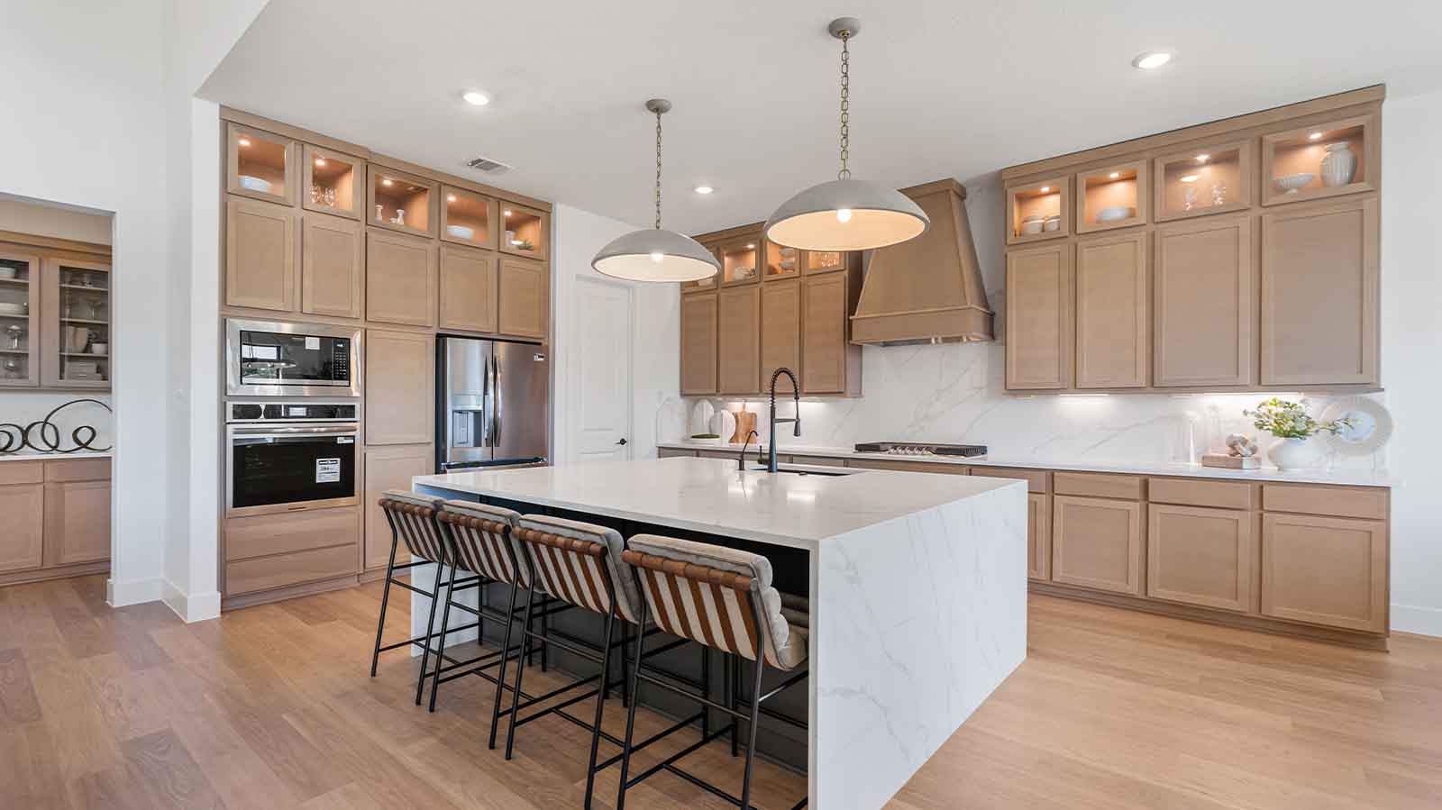 Luxurious and spacious kitchen with quartz countertops, stainless steel appliances,  stained wood cabinets, expansive storage and an island with bar seating.