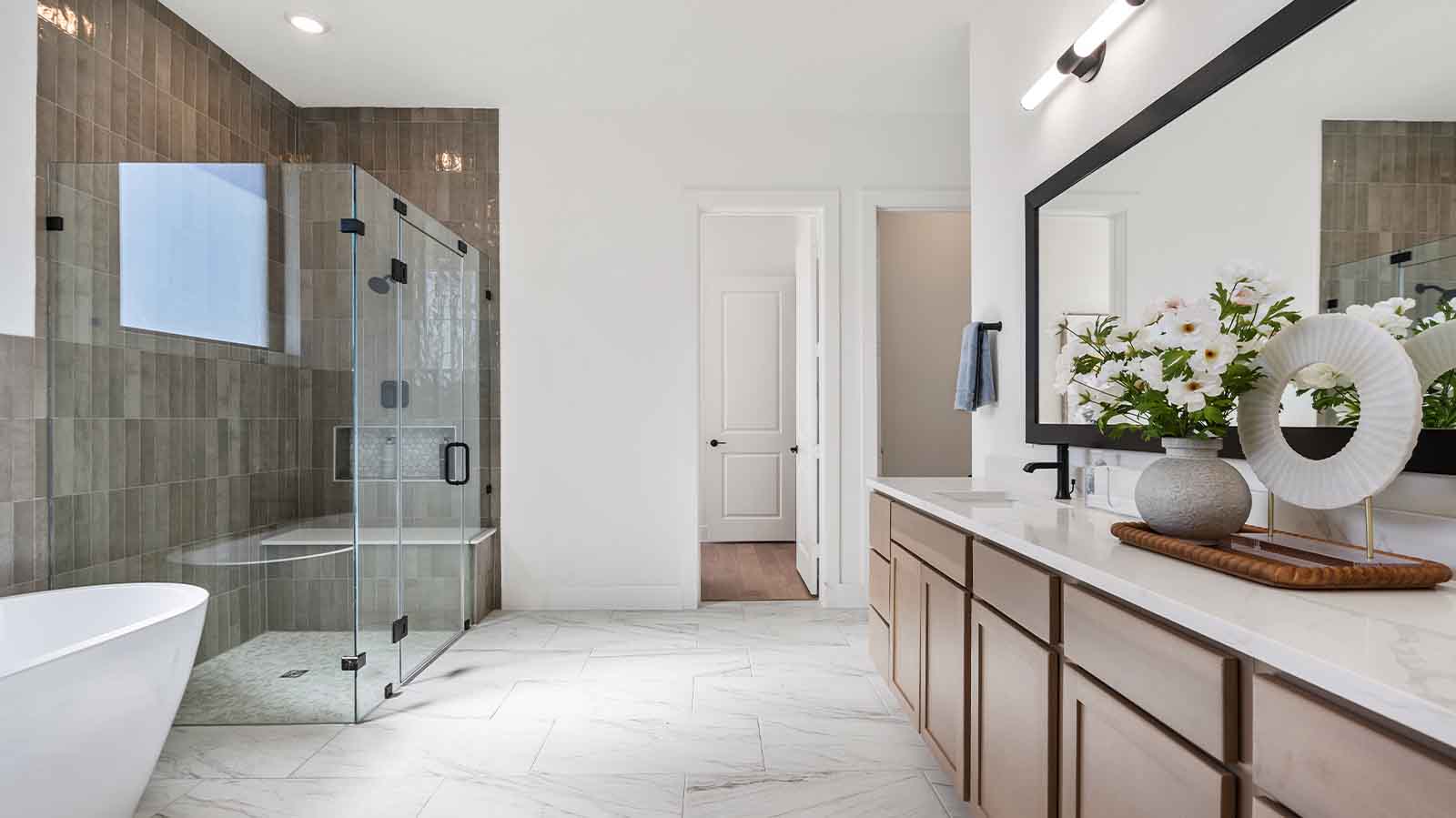 Luxurious primary bathroom with dual vanities, a soaking tub, and separate glass-enclosed walk in shower