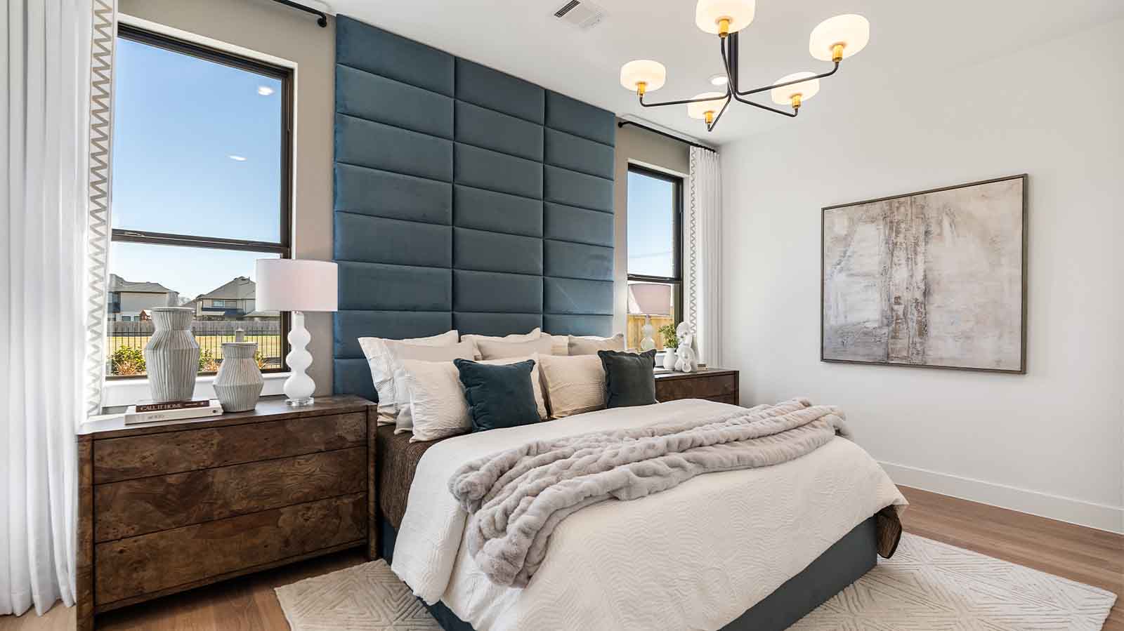 The primary bedroom with ceiling fan, three large windows for natural lighting, hardwood floors, and a large walk-in closet.