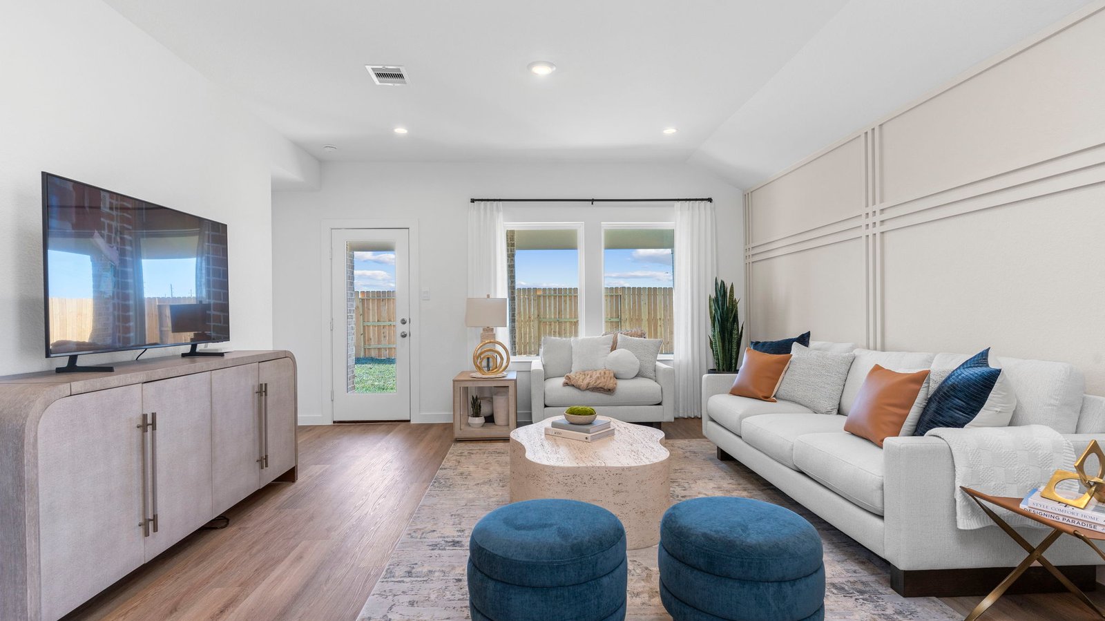 A cozy living room featuring large windows for natural lighting, wood flooring and a view to the kitchen and dining area.